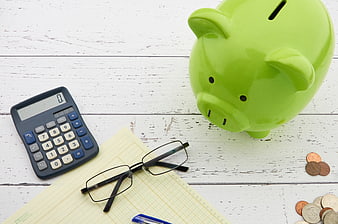 Green Piggy Bank, Calculator, and Coins on White Wood