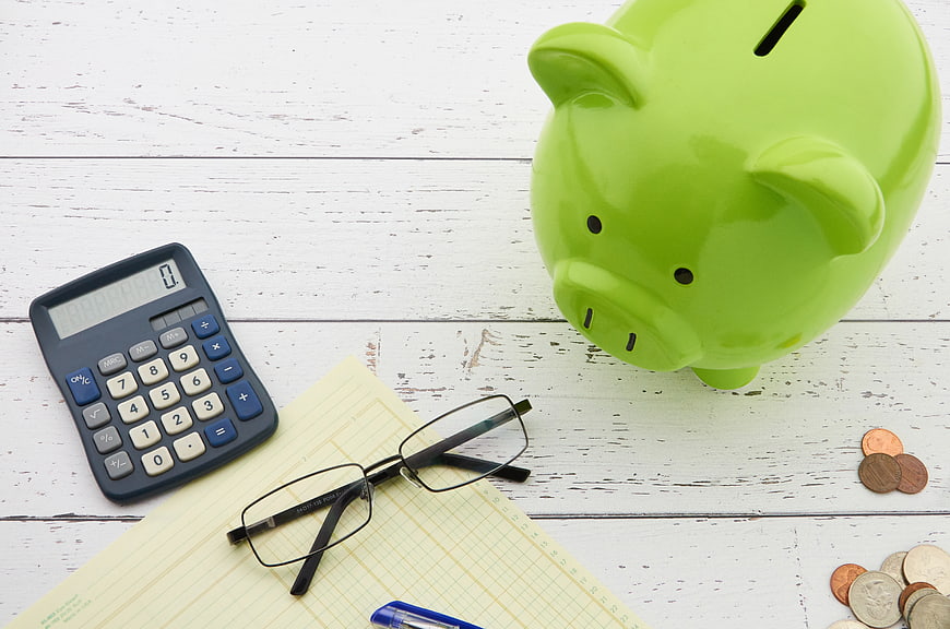 Green Piggy Bank, Calculator, and Coins on White Wood