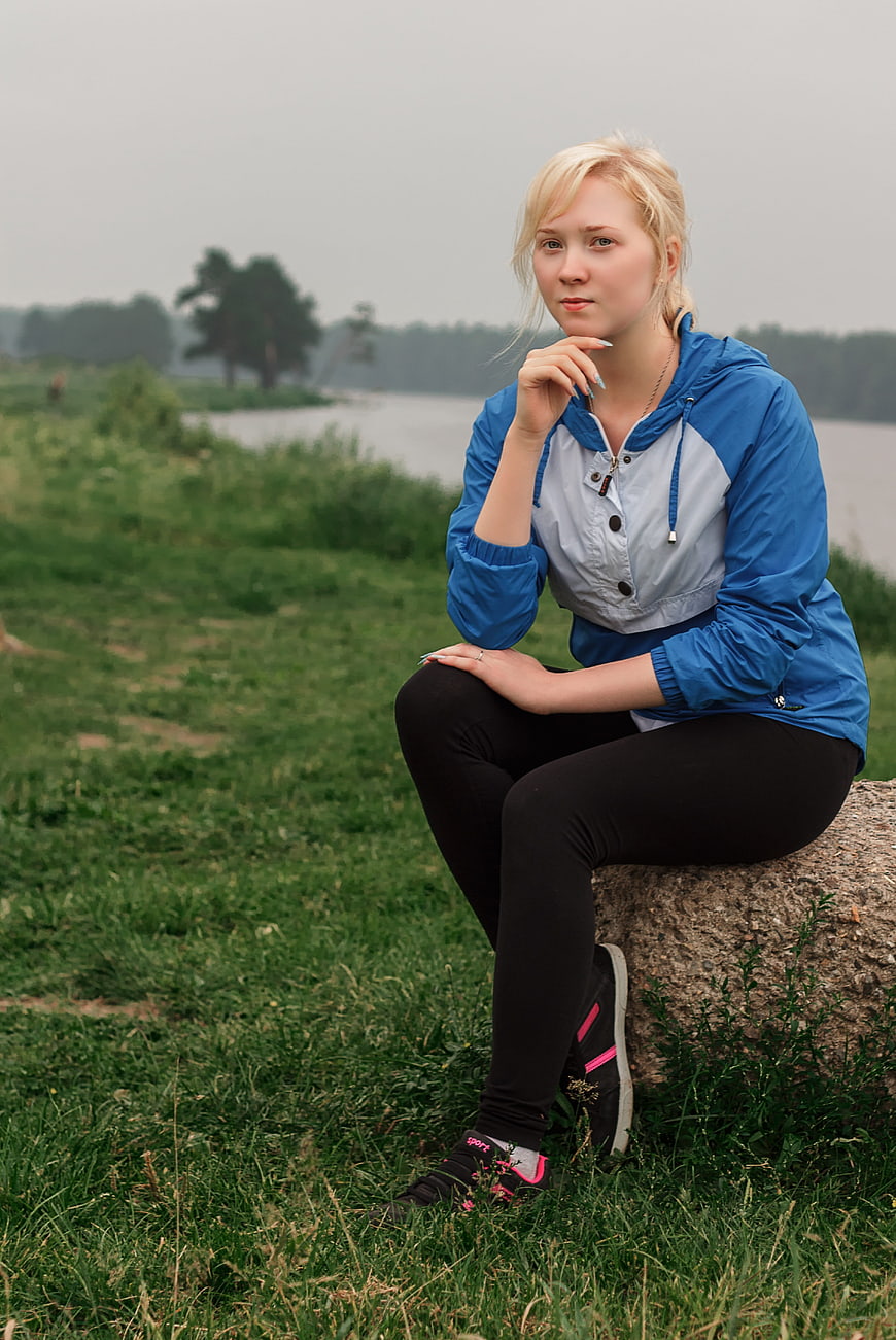 Young Blonde Woman Sitting on Rock by River