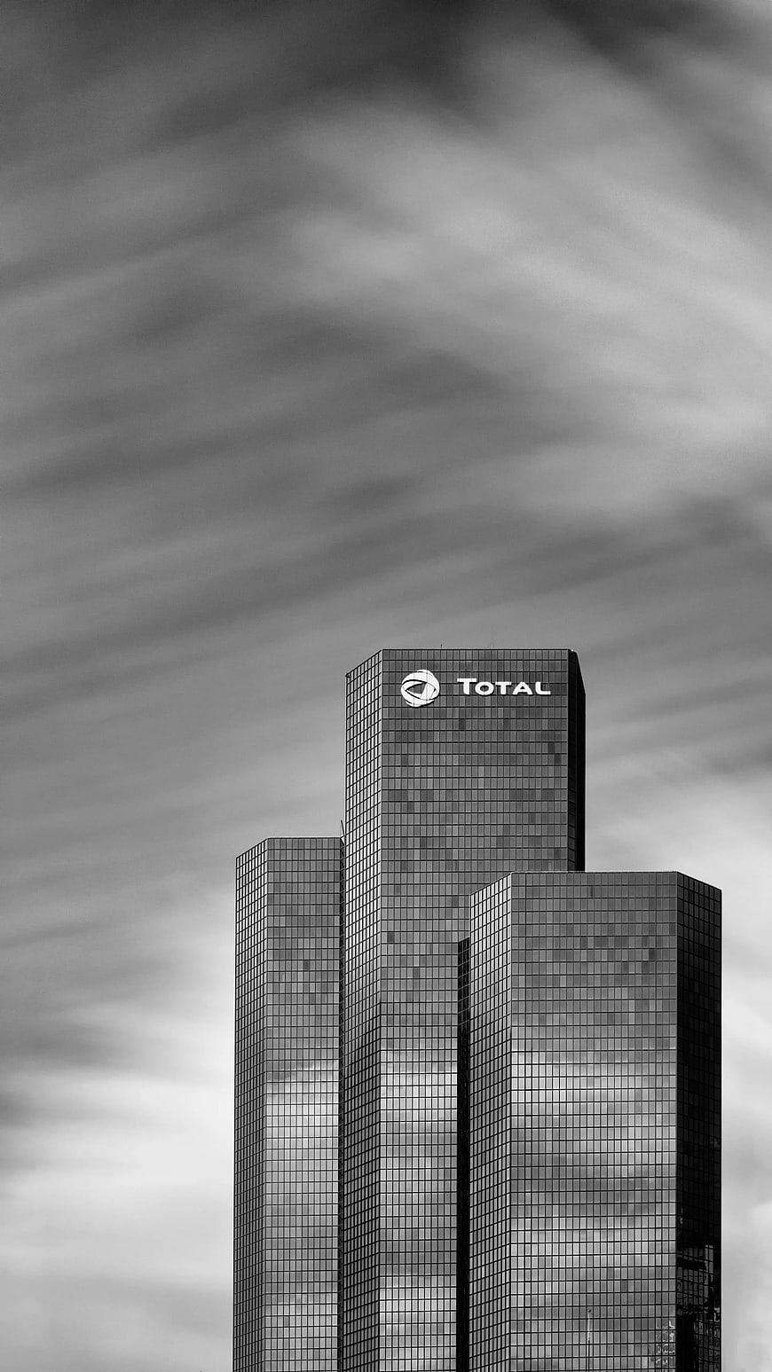 Black and white skyscraper with Total logo against cloudy sky