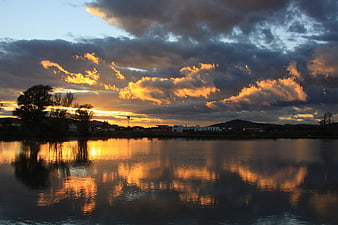 Dramatic Sunset Over Lake With Cloud Reflections And Distant Town