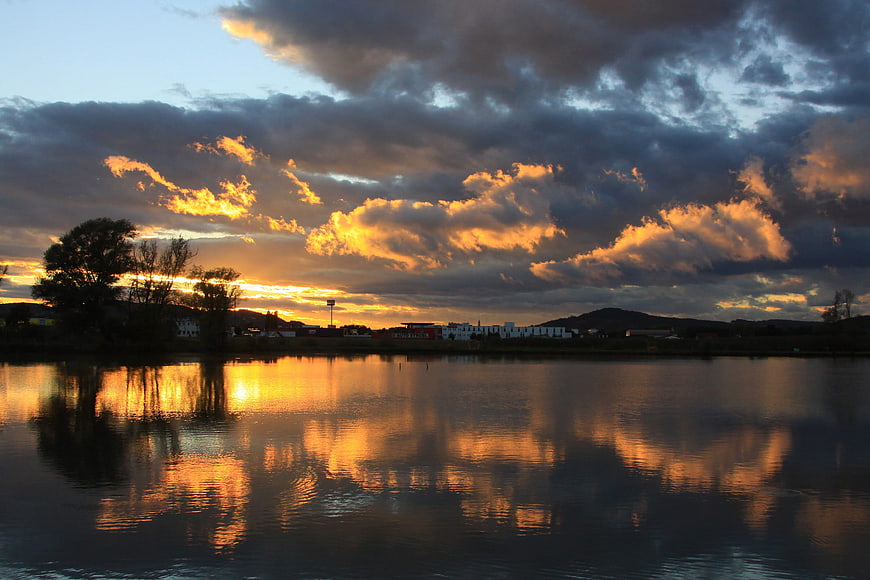 Dramatic Sunset Over Lake With Cloud Reflections And Distant Town