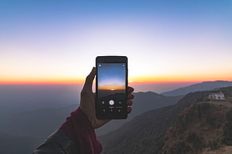 Hand holding smartphone capturing mountain sunset landscape