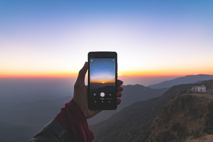 Hand holding smartphone capturing mountain sunset landscape