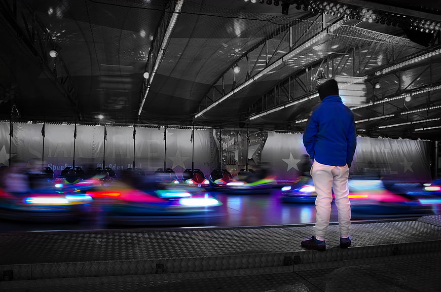 Man in Blue Jacket Watching Bumper Cars at Night