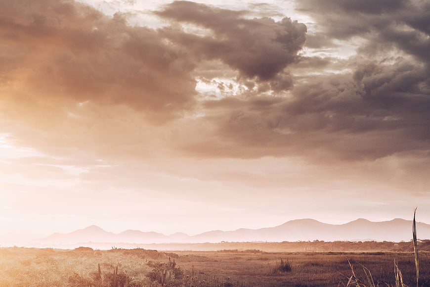 Dramatic sunset landscape with clouds over grassy field and mountains