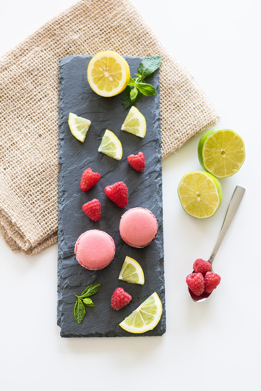Pink macarons with raspberries, lemon, and lime on slate