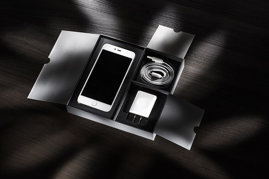 White Smartphone Unboxing with Charger and Cable on Dark Wood