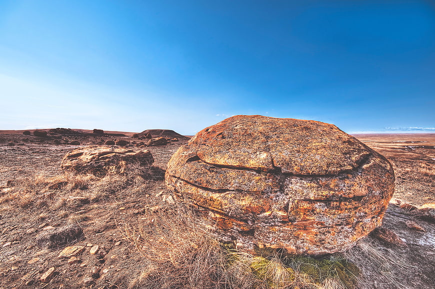 Large textured boulder in arid landscape under blue sky