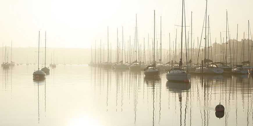 Sailboats in misty harbor at sunrise with calm water reflections