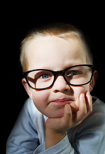 Portrait of a young boy wearing glasses with a black background