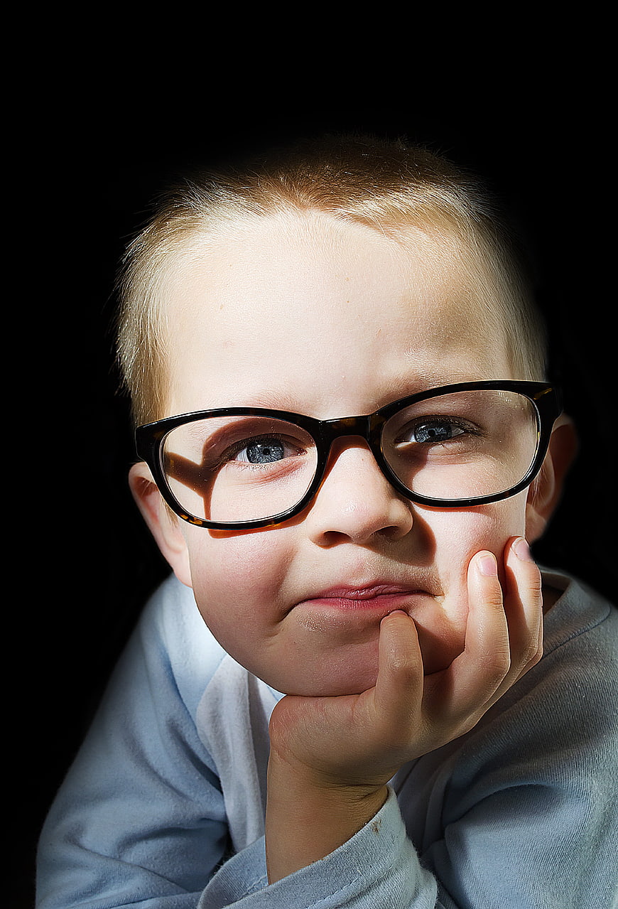 Portrait of a young boy wearing glasses with a black background