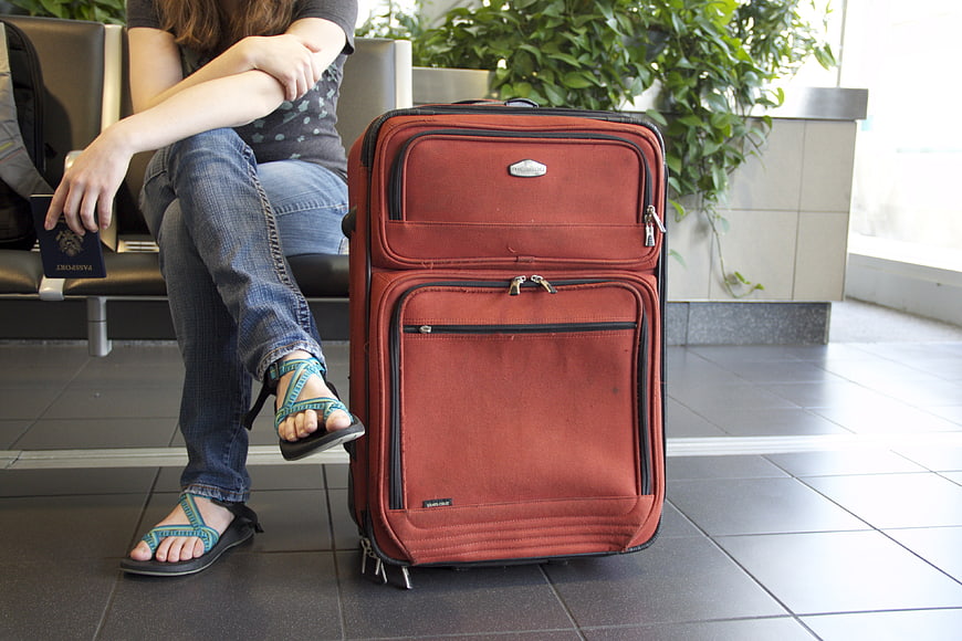 Woman with red suitcase and passport waiting at airport