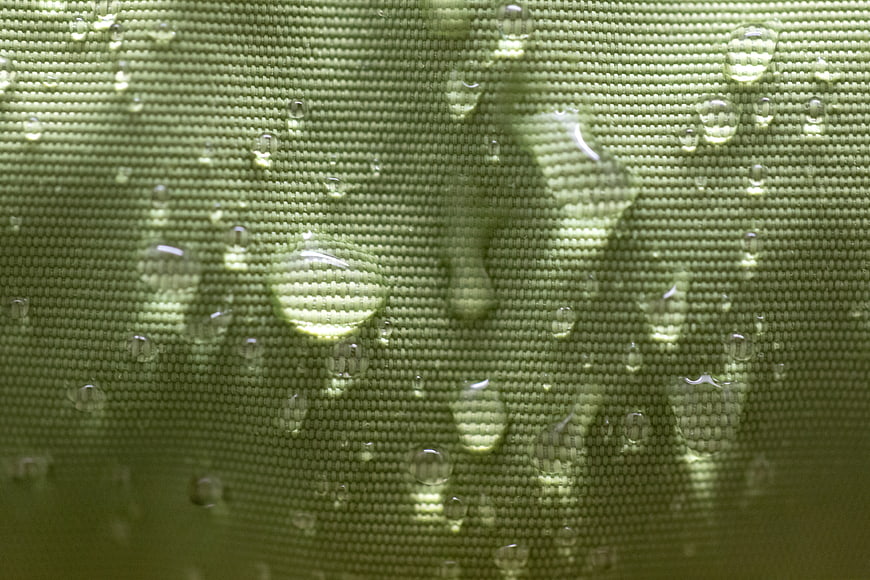 Macro shot of water droplets on green waterproof fabric texture