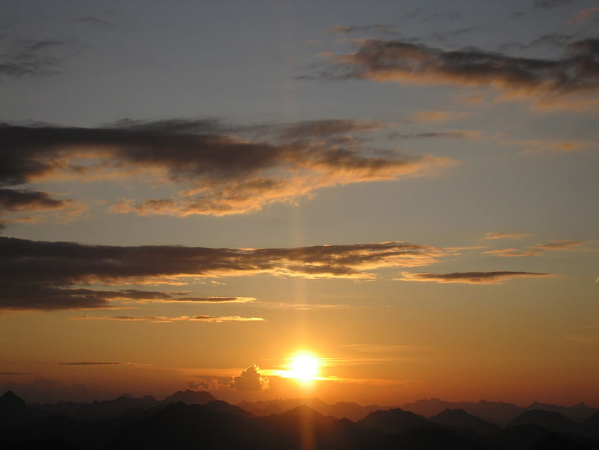 Golden sunset over layered mountain silhouettes with clouds