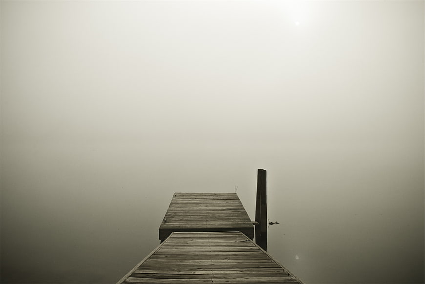 Minimalist wooden dock disappearing into thick fog on a calm lake