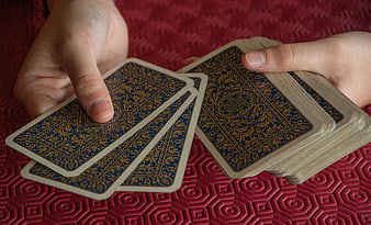 Hands holding blue and gold playing cards on red textured background