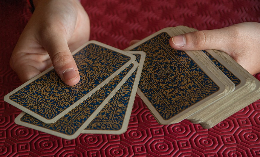 Hands holding blue and gold playing cards on red textured background