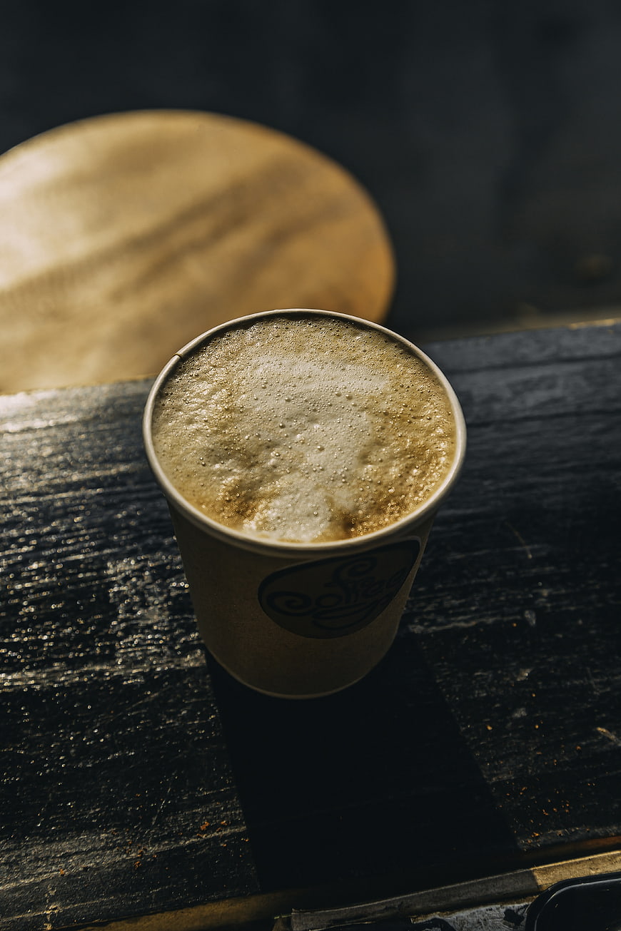 Top View of Foamy Coffee in Paper Cup on Dark Wood