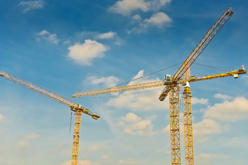 Yellow Construction Cranes Against Blue Sky With Clouds