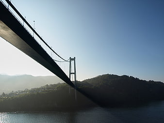 Silhouette of suspension bridge over misty water and hills