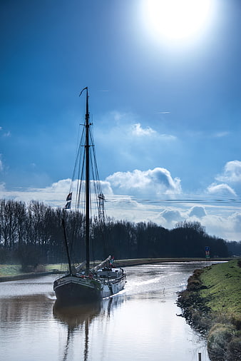 Traditional Sailboat Navigating a Canal Under Blue Sky