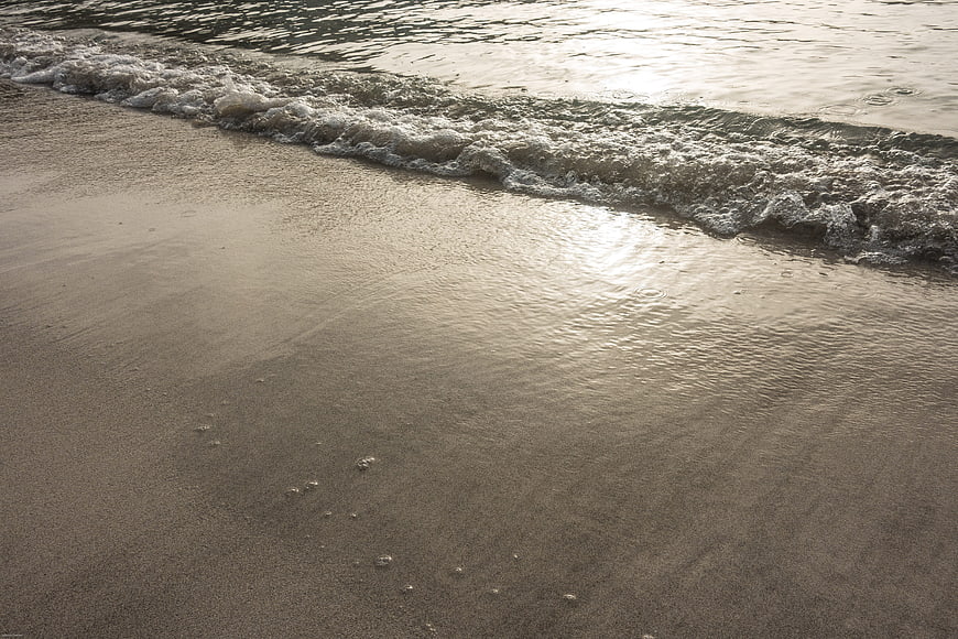Gentle ocean waves washing over wet sandy beach at sunset