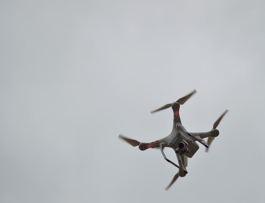 White Quadcopter Drone Flying Against Overcast Sky