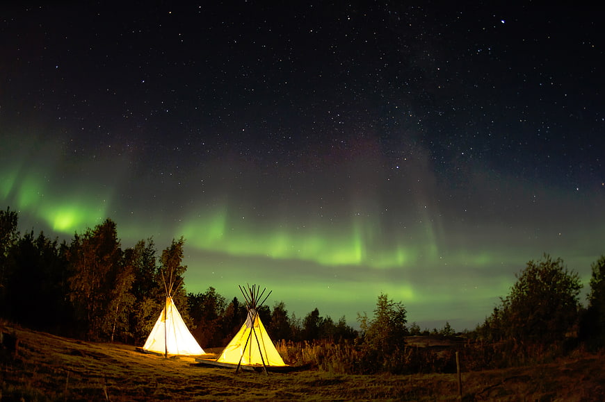 Illuminated Tents Under Northern Lights and Starry Night Sky