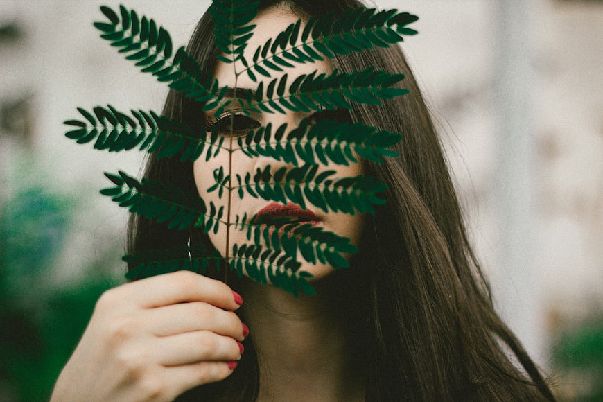 Woman holding green fern leaf over face