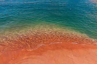 Aerial view of turquoise water meeting red sand beach