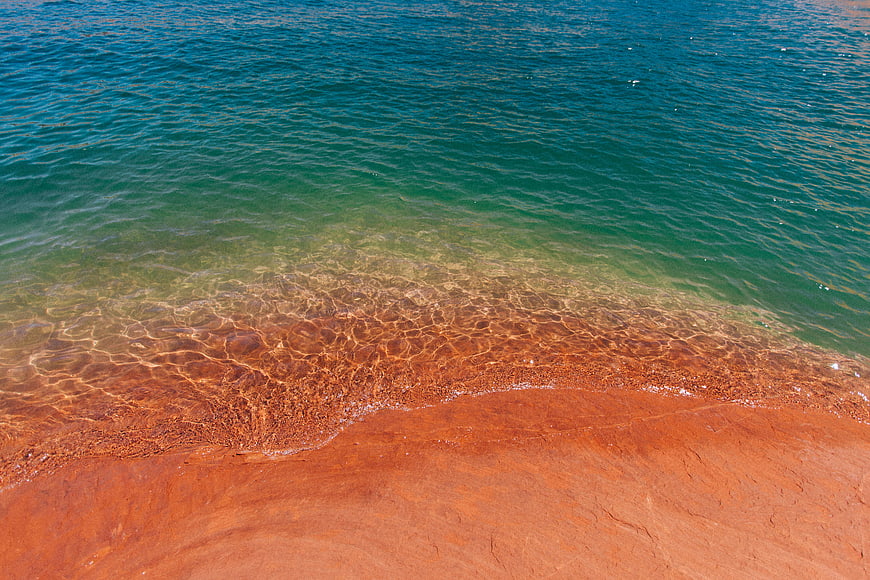 Aerial view of turquoise water meeting red sand beach