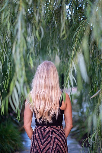 Woman with long blonde hair standing under willow tree branches