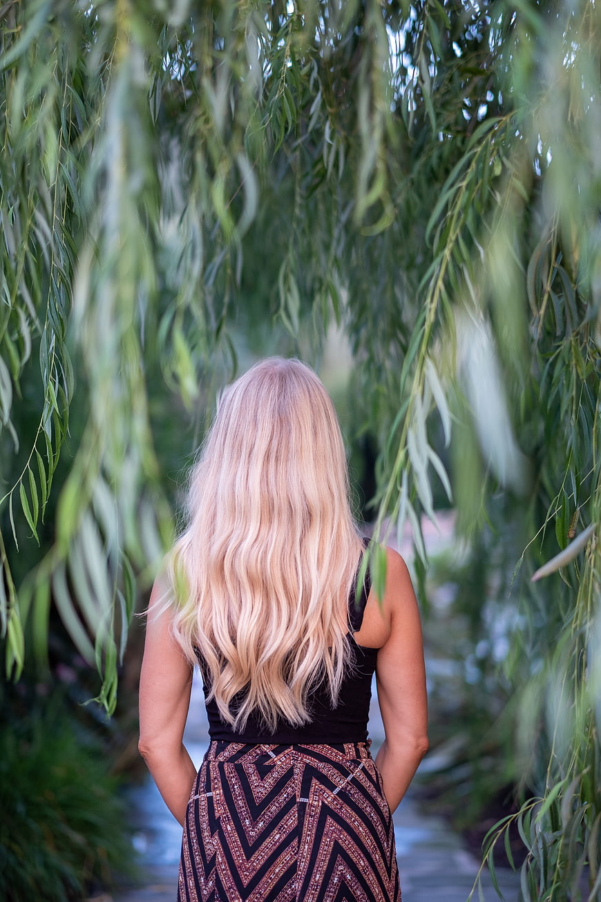 Woman with long blonde hair standing under willow tree branches