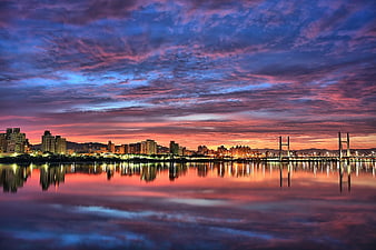 Vibrant Sunset Cityscape with Suspension Bridge and Water Reflection