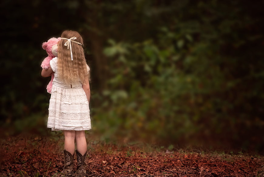 Little Girl in Cowboy Boots Holding Pink Teddy Bear in Forest