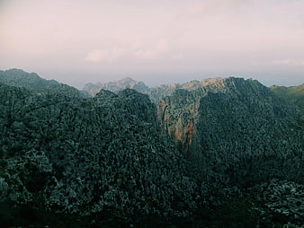 Dramatic jagged mountain peaks with forested slopes and soft sky