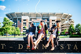 Three Female Graduates Celebrating With Champagne In Front Of Stadium