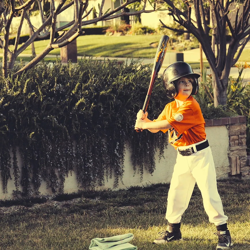 Young Boy in Baseball Uniform Holding Bat in Backyard