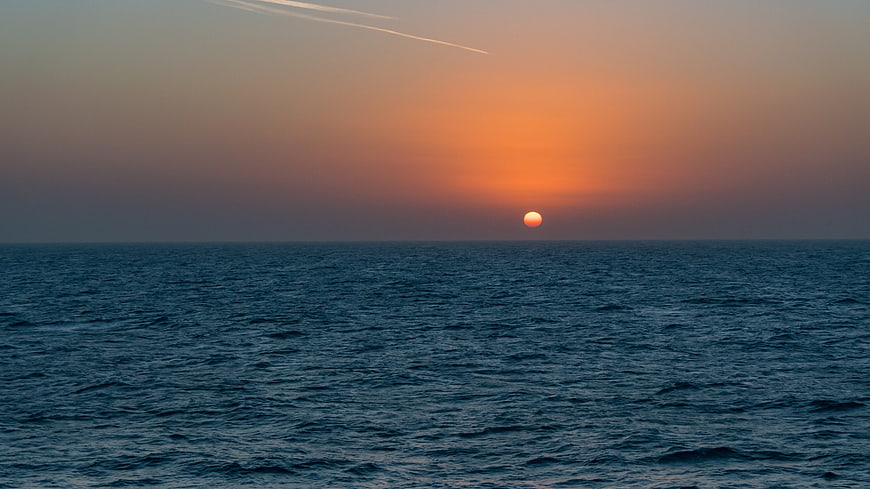 Serene Sunrise Over Calm Ocean with Contrails