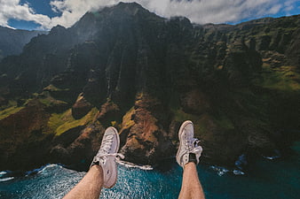 First-person view of legs in sneakers overlooking dramatic coastal mountains