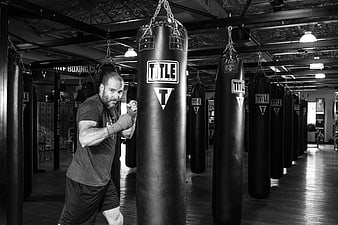 Bearded male boxer training with heavy bag in gym