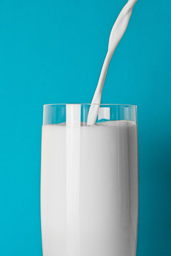 Fresh milk pouring into a glass on a blue background