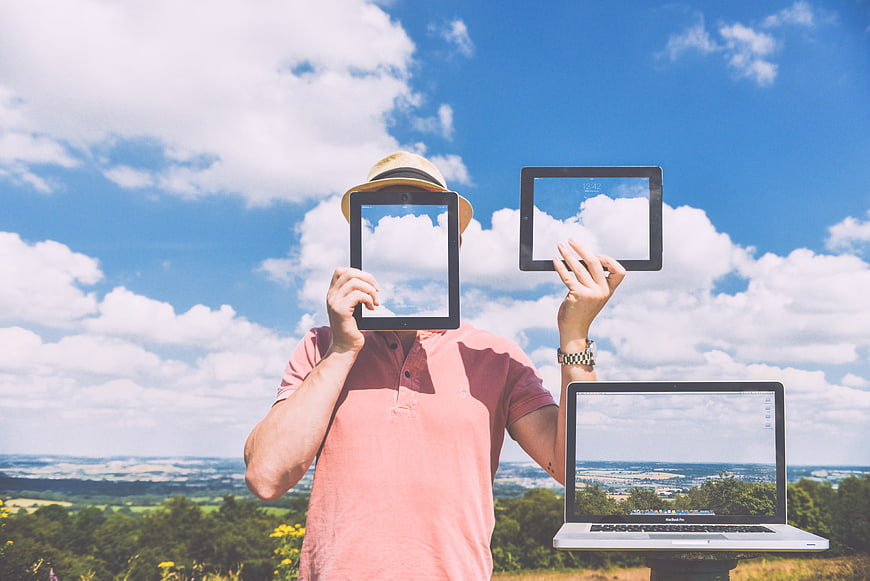 Man holding tablet and laptop outdoors with sky reflection