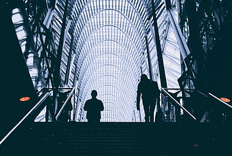 Silhouettes of people walking up stairs in modern glass architecture