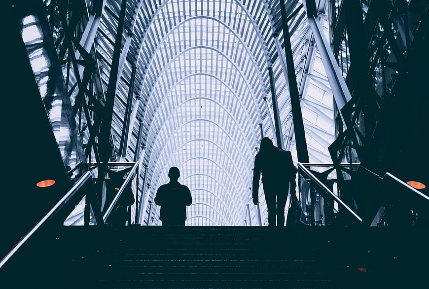 Silhouettes of people walking up stairs in modern glass architecture