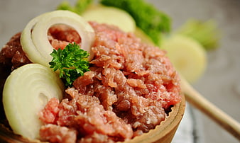 Raw minced meat with onion rings and parsley garnish in wooden bowl