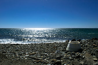 Rocks on pebble beach with sparkling blue sea horizon