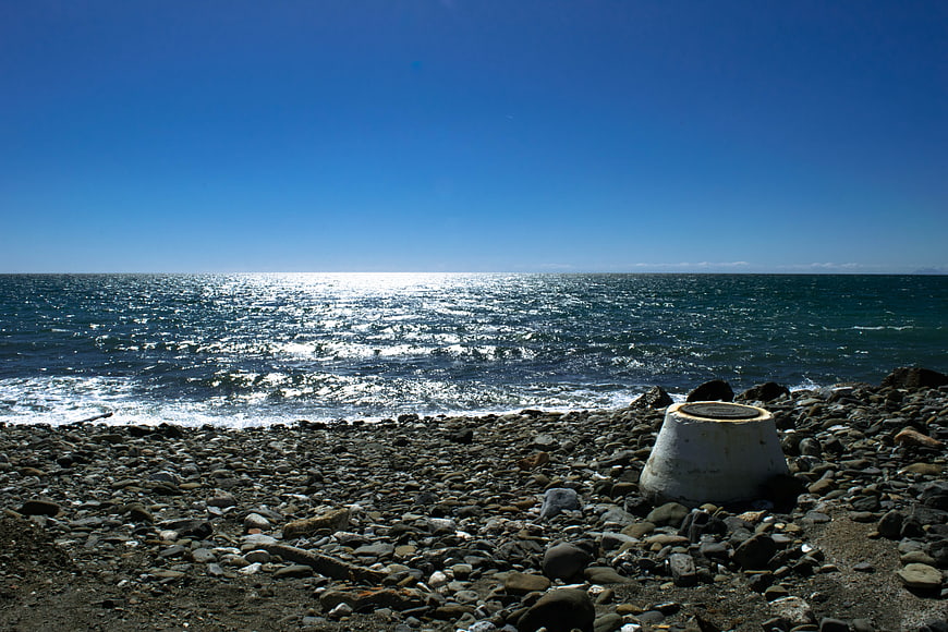 Rocks on pebble beach with sparkling blue sea horizon