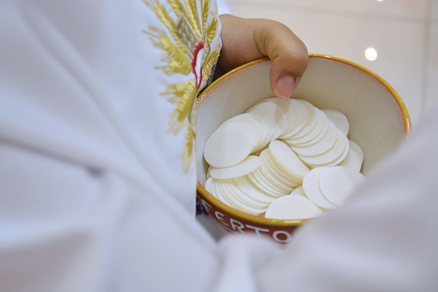 Catholic priest holding bowl of communion hosts